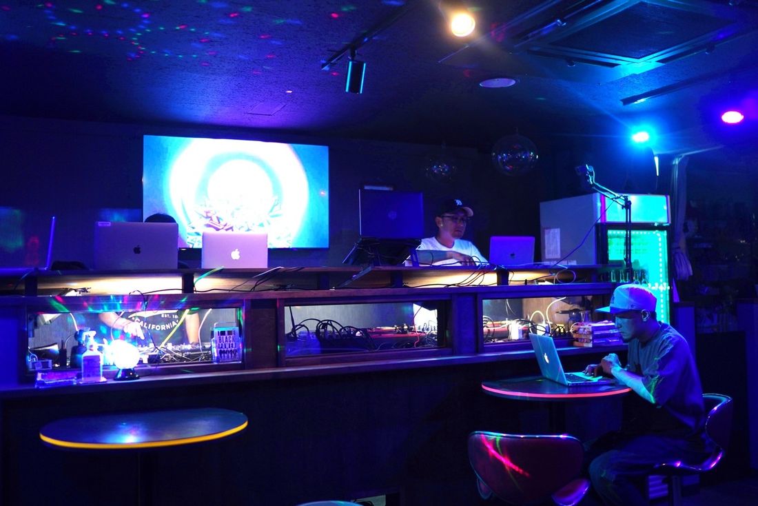 ラップトップを開いてくつろぐ来店客とDJブース